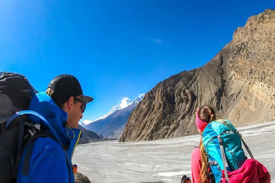 Two trekkers looking across a dry glacial valley toward a snow peak in Nar Phu