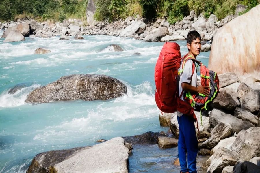 A lone trekker with a backpack beside a turquoise glacial river on the Kanchenjunga trail