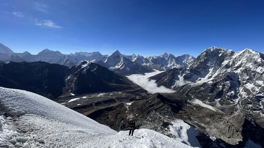 A lone climber high on a snowy Himalayan ridge above a cloud-filled valley