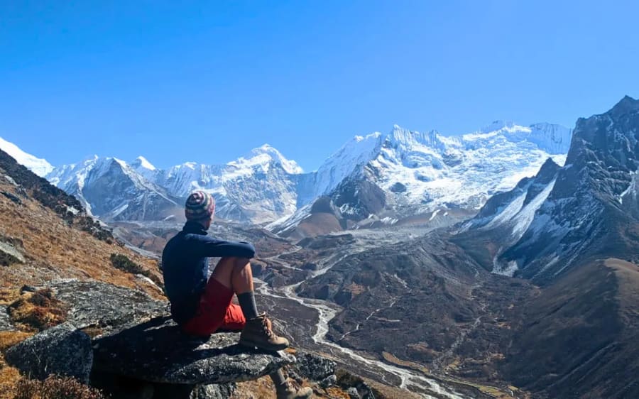 A trekker resting on a rock above a glacial valley of snow peaks in the Everest region