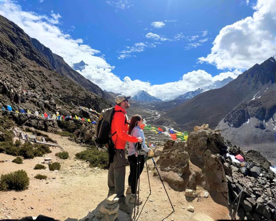 Trekkers walking a rocky Everest-region trail with prayer flags and Ama Dablam behind