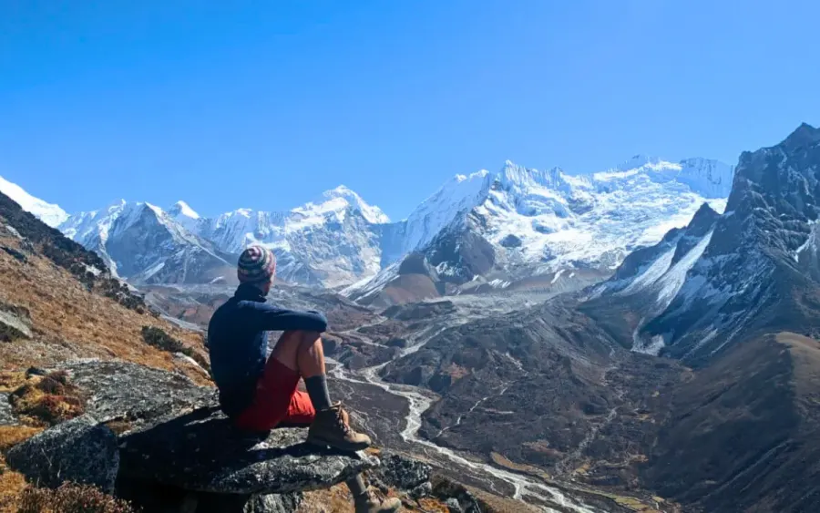 A climber resting on a rock above a glacial valley of snow peaks in the Everest region