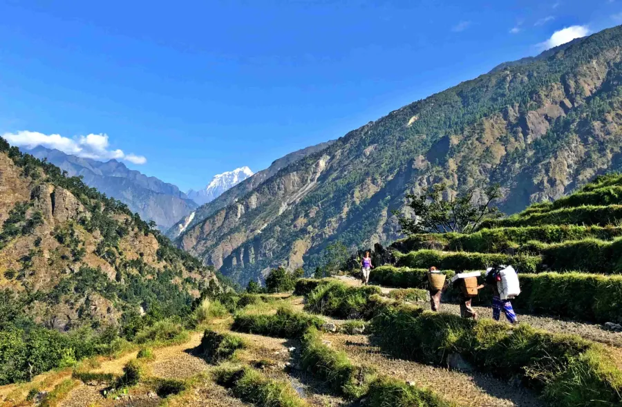 Trekkers and a porter on a terraced trail in the lower Manaslu valley